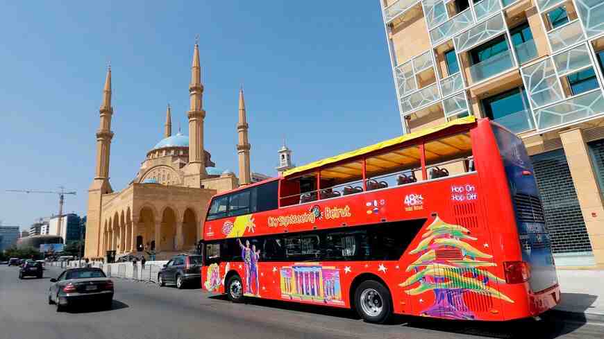 A red tourist bus in front of a mosque in the city of Beirut