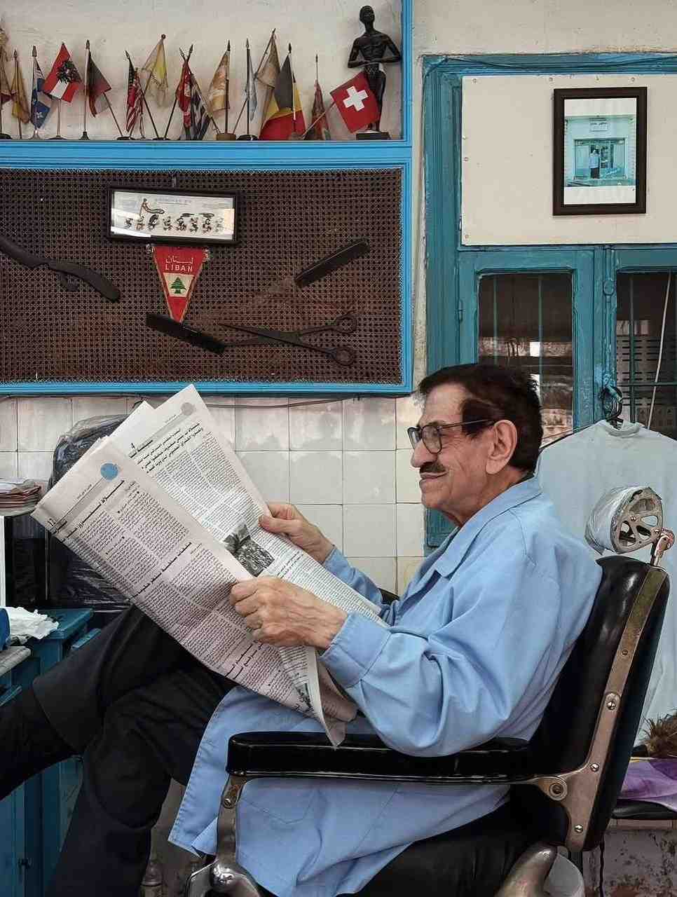 An older Lebanese barber sits comfortably on his chair in his shop