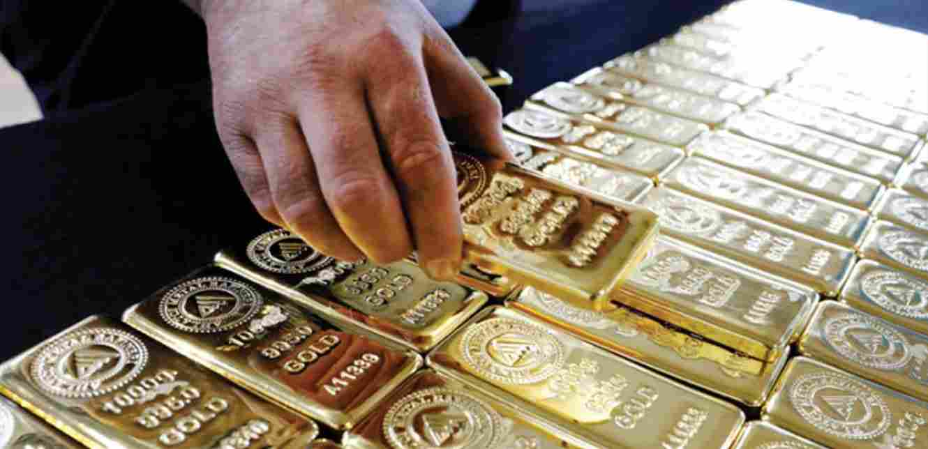 يد تمسك قطعة ذهب فوق أكوام الذهب المكدس