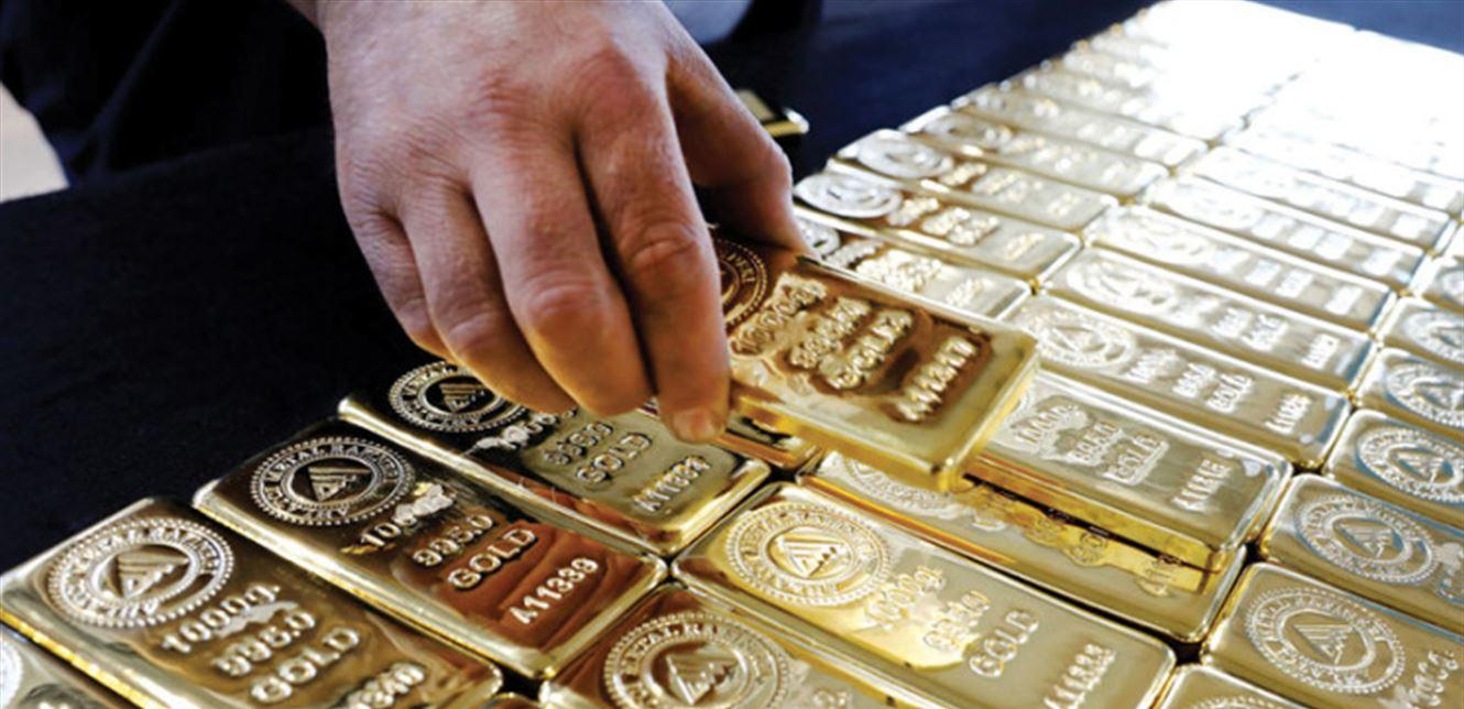 Hand holding a gold bar over stacked bullion Hand holding a gold bar over stacked bullion